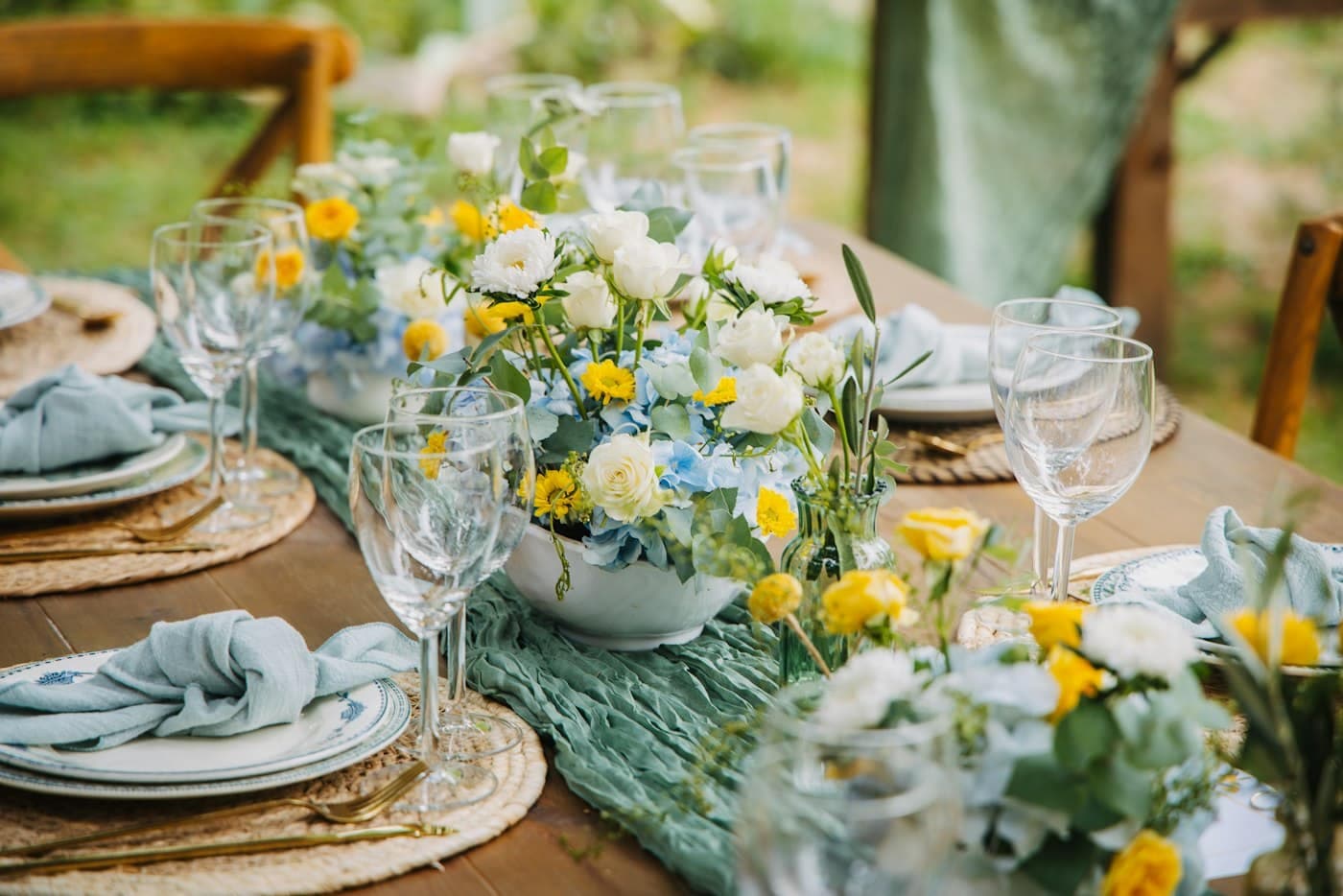 Mesa puesta con flores blancas y amarillas, copas y servilletas azules