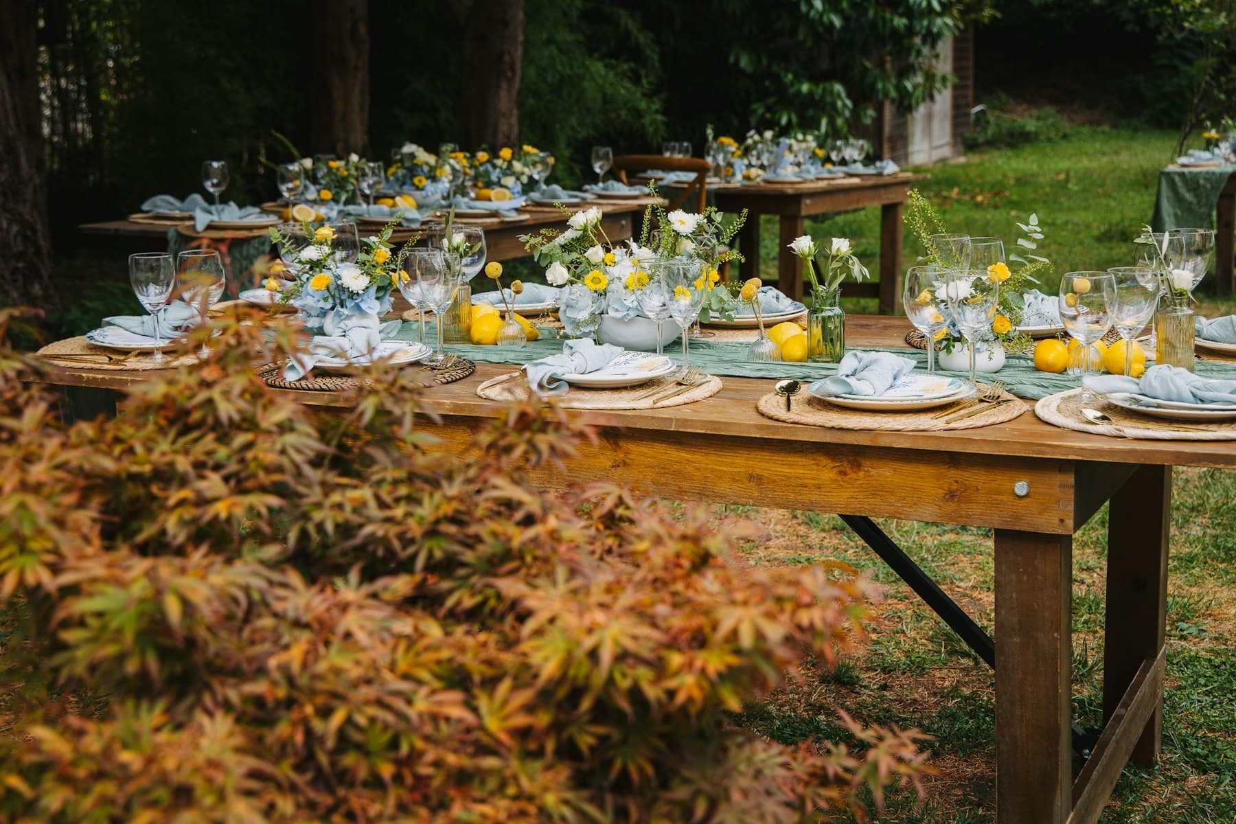 Mesas largas de madera puestas para un banquete en el jardín