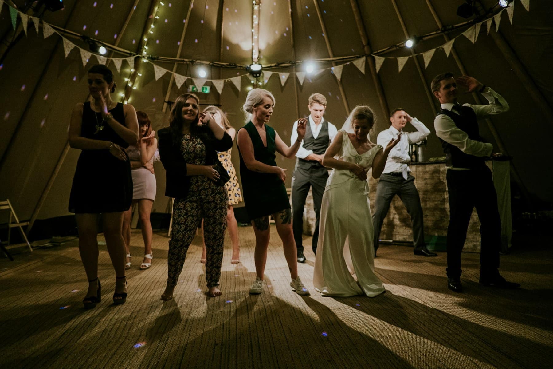 Invitados bailando de noche bajo una carpa con banderines y luces
