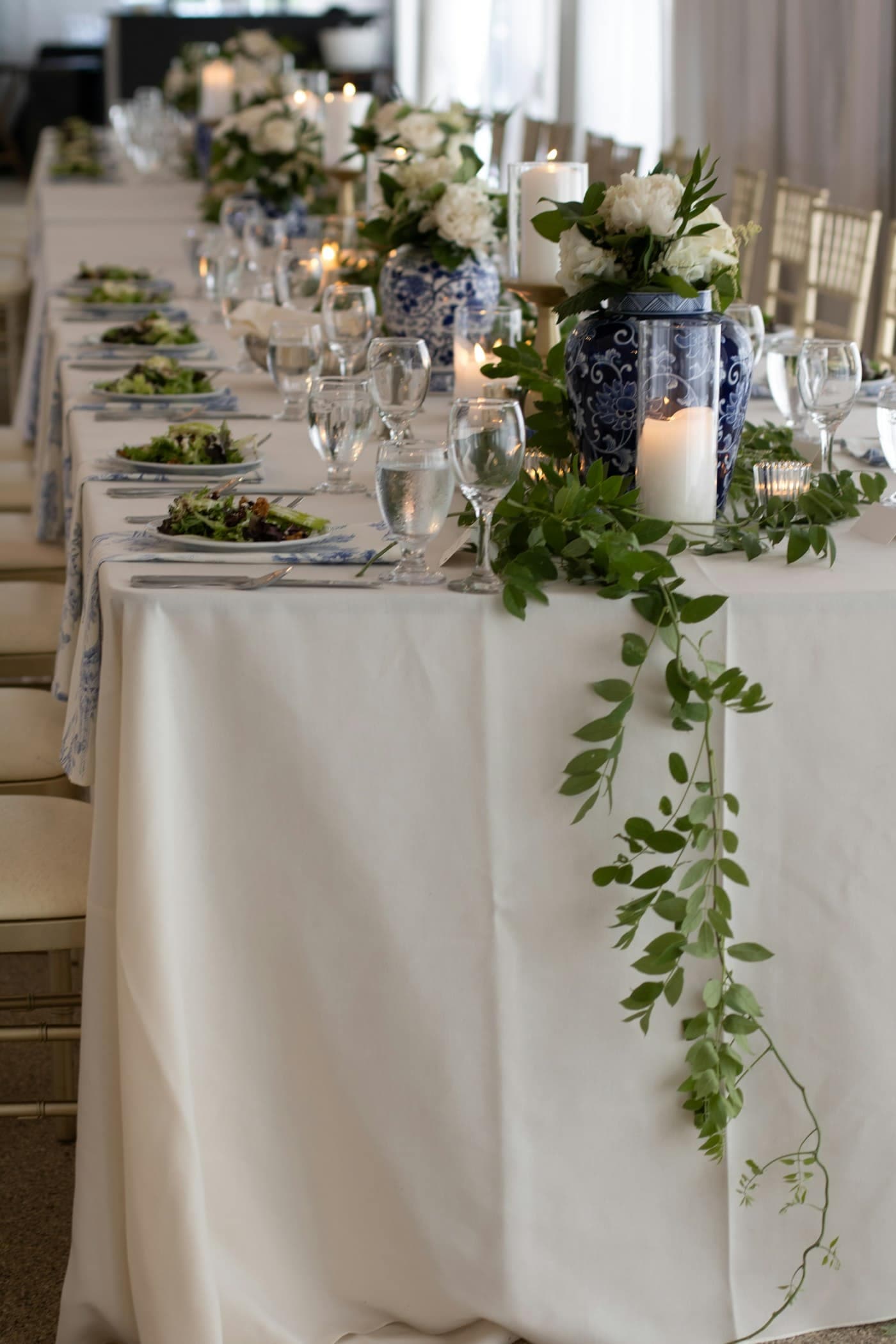 Mesa con mantel blanco, velas y guía de hojas verdes